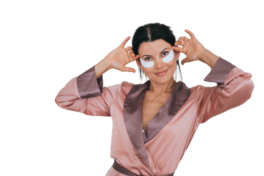Brunette hispanic woman in silk robe with patches on face looks at camera against transparent background. Satisfied caucasian female happy after spa procedure. Healthcare, skin care, women life.