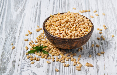 Peeled cedar nuts in a wooden cup on a white wooden background. Rustic style. The concept of vegetarian and diet snacks.