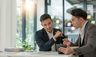 Two business people talk project strategy at office meeting room. Businessman discuss project planning with colleague at modern workplace while having conversation and advice on financial data report.