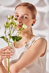 A young woman with special needs with flowers in her hand, a girl born without a hand, in white dress on a white background in the rays of the sun beauty fashion concept