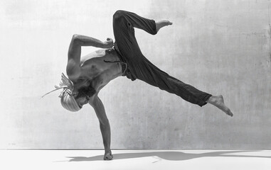 Black and white image, monochrome. Muscular body. Shirtless sportive man training, practising yoga over textured background. Art of movement, male body aesthetics, health, sportive lifestyle concept