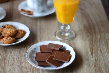 Cup of tea or coffee, plate of cookies, cup of blueberries, plate of chocolate, glass of juice, book, reading glasses, teapot, flowers and lit candles on the table. Brunch or afternoon tea concept. 
