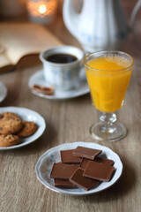 Cup of tea or coffee, plate of cookies, cup of blueberries, plate of chocolate, glass of juice, book, reading glasses, teapot, flowers and lit candles on the table. Brunch or afternoon tea concept. 