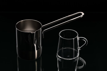 Metal shiny cezve and glass cup on a black background.