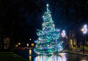 Colorful decorated Christmas tree in the river at Bourton-on-the-Water in The Cotswolds