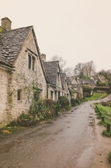 Fototapeta na wymiar Wet road running alongside a row of historic quintessential Cotswold cottages in Bibury, England