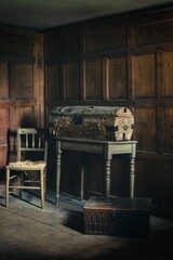 Vertical shot of an old dusty money chest next to a chair in a room with wooden walls