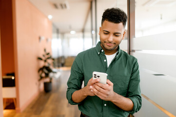 Handsome hispanic guy is using smartphone for messaging, texting, young indian man in smart casual...