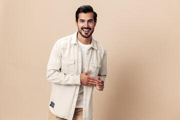 Stylish male smile model posing on a beige background in a white t-shirt looking at the camera,...