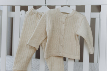 Set of merino wool organic baby clothes with hanger on bed. Present for cold weather. Newborn gifts...
