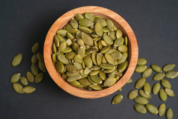 Pumpkin seeds in a wooden bowl on a dark background