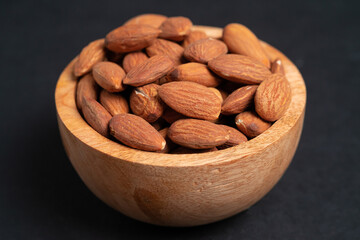 Almonds in wooden bowl on black background