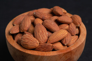 Almonds in wooden bowl on black background