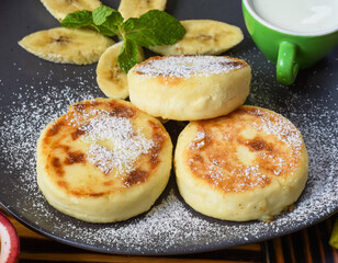 Syrniki or cheese pancakes with cream sauce and bananas on a plate on wooden table close up