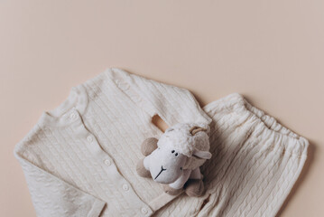 Sheep toy on stack of merino wool baby clothes over beige background. Present for cold weather....