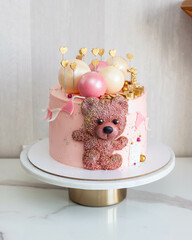Tender pink cake for baby girl birthday with chocolate spheres, cute fondant teddy bear toy, golden...