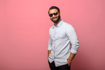 Handsome bearded Indian man wearing sunglasses in casual jeans shirt looking at camera and smiling...
