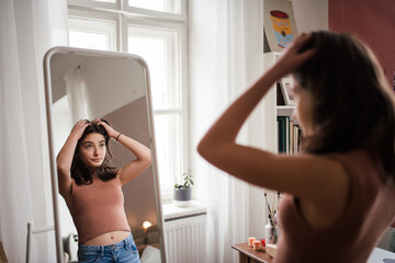 Young teenage girl looking in the mirror in her room.