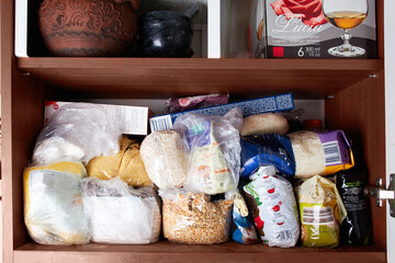 Unorganized storage of cereals in the kitchen cabinet. Macaroni, sugar, buckwheat, corn balls in sack bags.