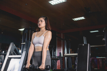 Fototapeta na wymiar A serious young woman does a set of front dumbbells raises. Training and toning shoulder muscles at the gym.