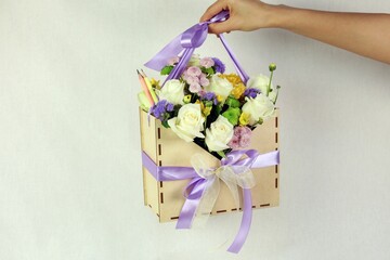 Person holding a brown gift box containing a bundle of colorful flowers tied together with a  ribbon