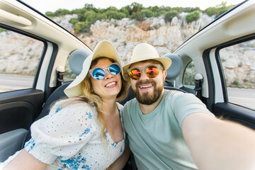 Romantic couple making selfie on smartphone camera in rental cabrio car on ocean or sea beach...