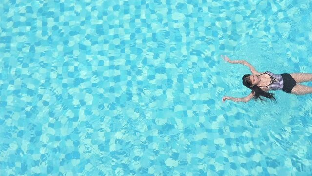 Top view of a female athlete swimming using a backstroke technique in a clear bright blue pool