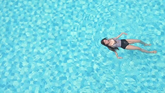 Aerial shot of a girl swimming in the backstroke technique in a clear blue pool