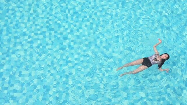 Skilled female swimmer doing a backstroke in a bright, clear blue pool on a hot summer day