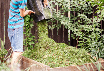 Gardener Throwing Grass from Lawn Mower into Compost Bin in Garden. Preparing Compost, Recycling...