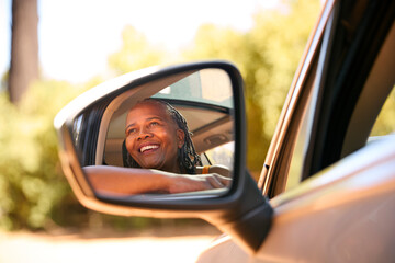 Smiling Senior Female Driver Looking Out Of Car Window Enjoying Day Trip Out Driving