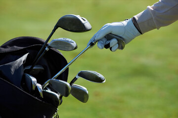 Closeup of unrecognizable golf player choosing club and taking out of golf bag against green grass...