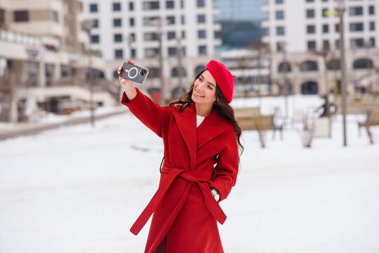 a beautiful girl in a red coat and a red beret takes a selfie in the winter with a phone