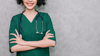 Portrait doctor hanging stethoscope standing on grey loft background, Professional nurse wearing green scrub uniform while arm crossed, Medical and healthcare concept.