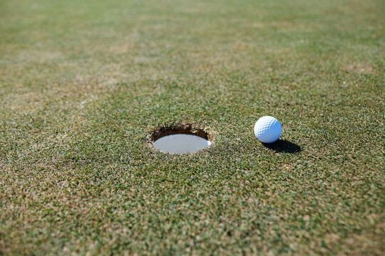 Close up background image of golf ball next to hole on green grass, copy space