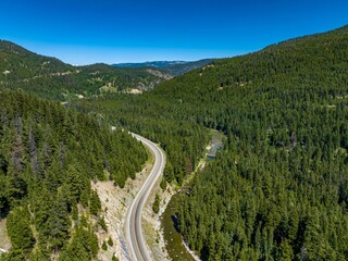 Fototapeta na wymiar Drone view of Crowsnest Highway by river passing through rocks, dense forests and mountains, Canada.