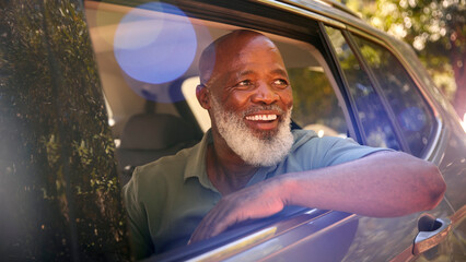 Smiling Senior Male Passenger Looking Out Of Back Seat Car Window Enjoying Day Trip Out Driving
