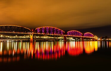 Fototapeta na wymiar Big Four Bridge reflecting on a river, illuminated at night in Louisville, Kentucky
