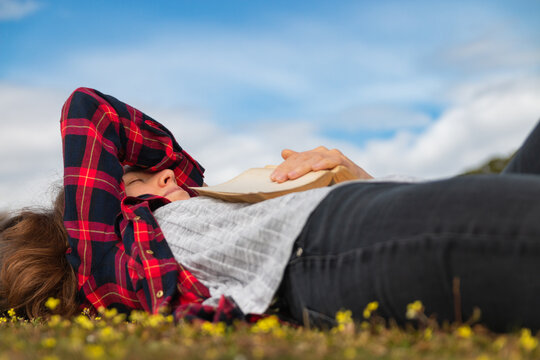 Young woman laying and sleeping on the grass holding a book