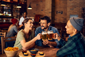 Young cheerful people toasting with beer while gathering in pub.