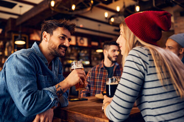 Happy man drinking beer and talking to female friend in pub.