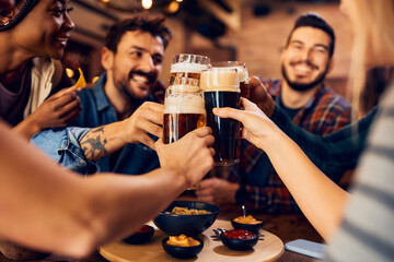 Close up of friends toasting with beer in pub.
