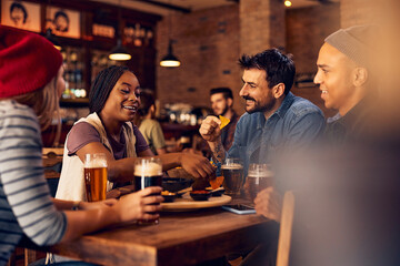 Group of happy multiracial friends enjoy in nacho chips and beer in bar.