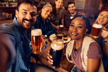 Cheerful friends taking selfie while drinking beer in pub.