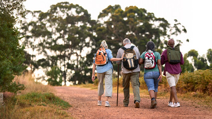 Obraz premium Rear View Of Active Senior Friends Enjoying Hiking Through Countryside Walking Along Track Together