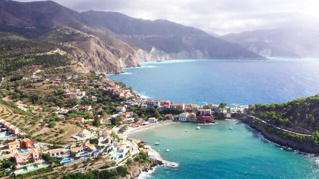 Colorful fishing Asos village houses picturesque flyiing drone aerial 4K shot on Cephalonia island, Greece. Steep cliff banks washed by blue Ionian Sea waves.
