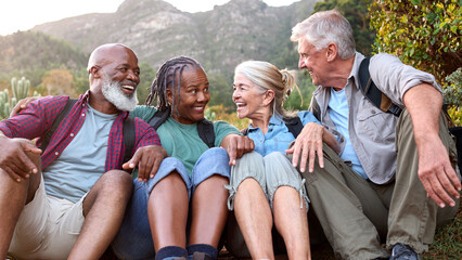 Active Senior Friends Sitting Taking A Break Hiking Through Countryside Together