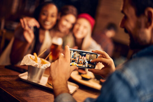 Close up of man photographing his friends with mobile phone in pub.