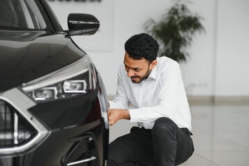 Indian man adult customer male buyer client wears classic suit white shirt chooses auto wants to buy new automobile touch check car in showroom vehicle salon dealership store motor show indoor.