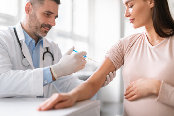Vaccination in pregnancy. Pregnant woman getting vaccinated, male doctor giving vaccine shot injecting lady in arm